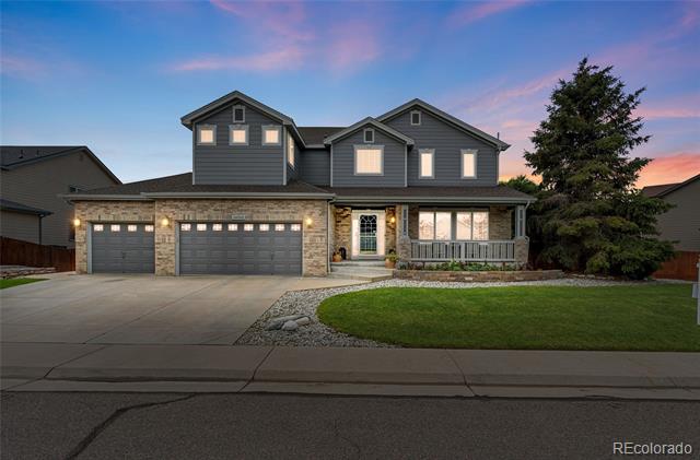 Two-story gray home with stone accents, three-car garage, and front lawn at dusk.