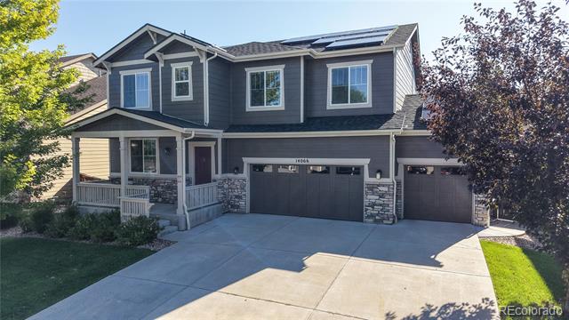 Two-story gray house with a covered porch, stone accents, solar panels, and a wide driveway.