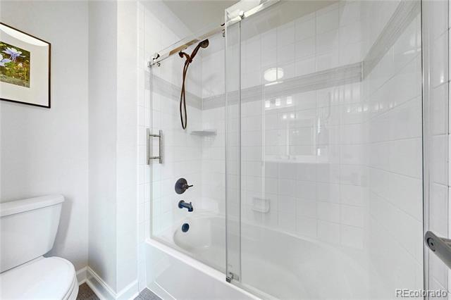 Bathroom with a white tiled tub and shower enclosed by clear glass.