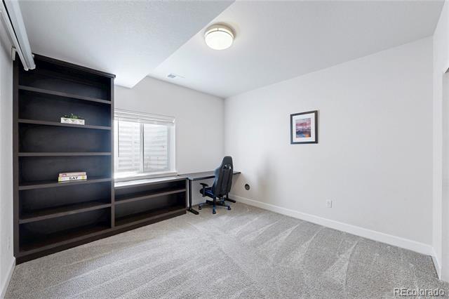 Bright home office with dark built-in shelving and desk, office chair, and window with white blinds.