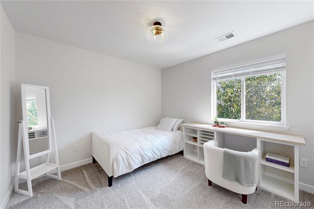 Bedroom with a white bed and desk beneath a window overlooking leafy trees.