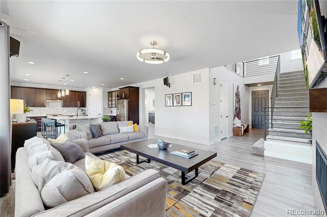 Open-plan living room with gray sectional sofas, a dark coffee table, and a staircase beside the entry.
