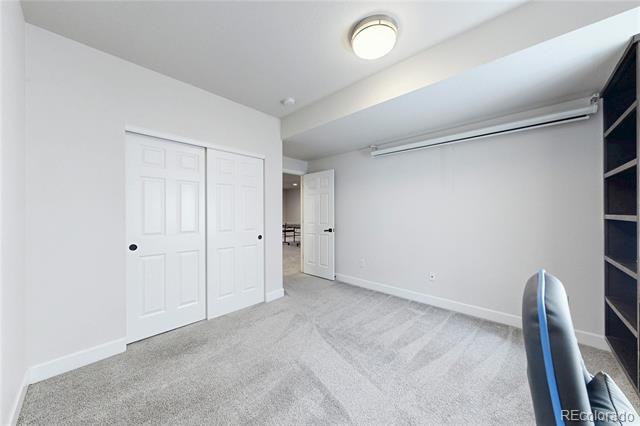 Empty carpeted room with white closet doors, built-in shelving, and a blue office chair at the edge.
