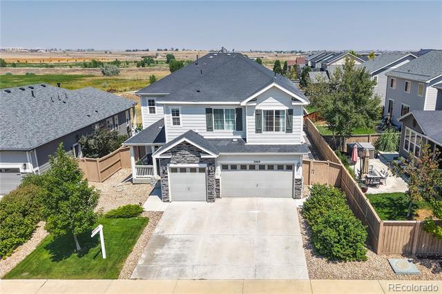 Aerial view of a two-story gray house with a covered porch, two-car garage, and fenced patio.