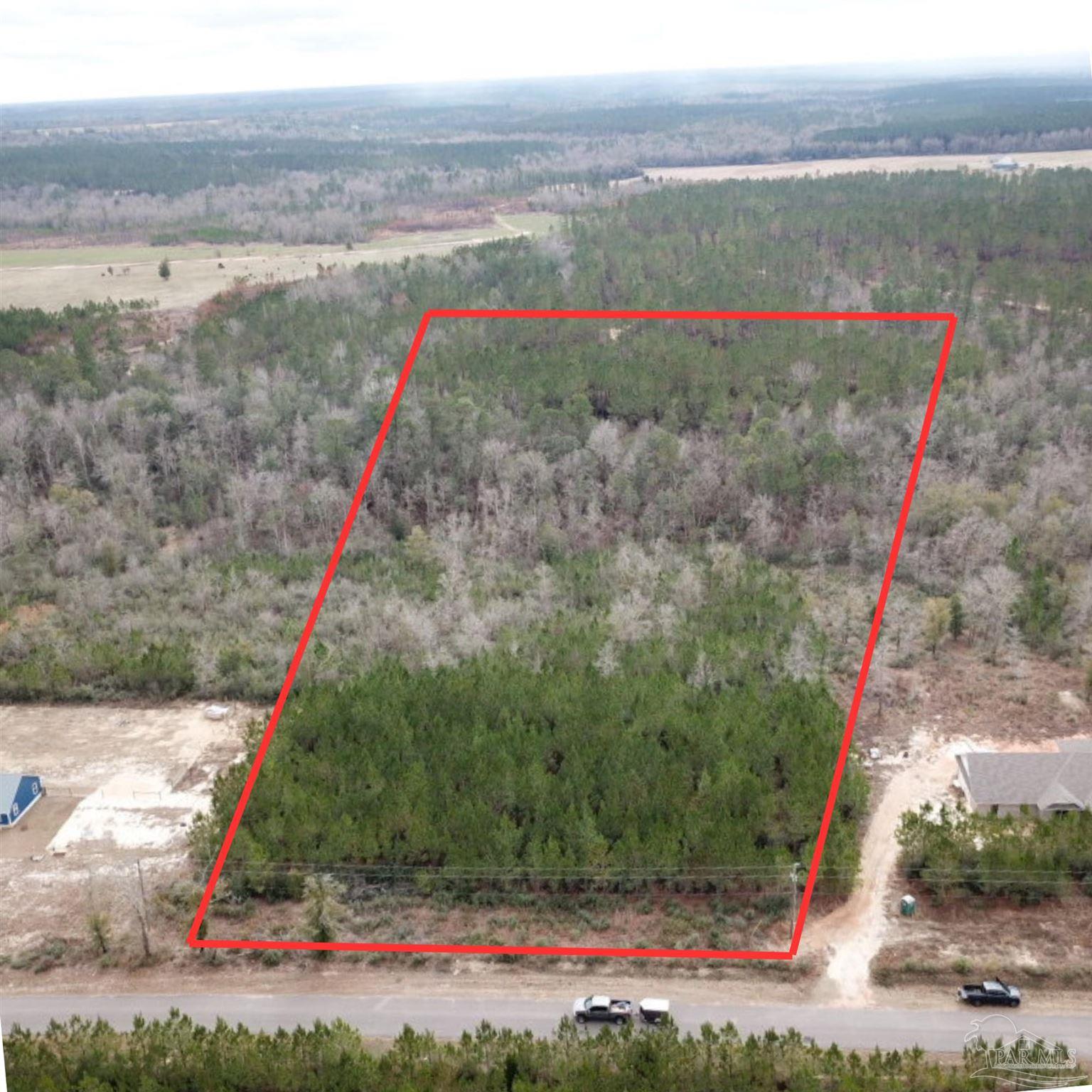 Wooded vacant lot outlined in red, beside a road and neighboring homes.