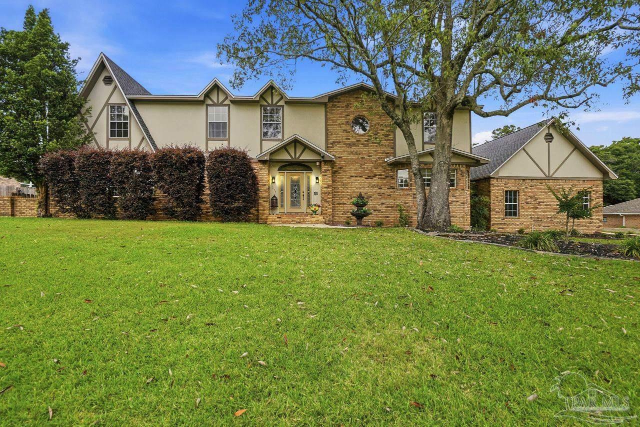 Two-story Tudor-style home with brick and stucco exterior, broad lawn, and mature tree.