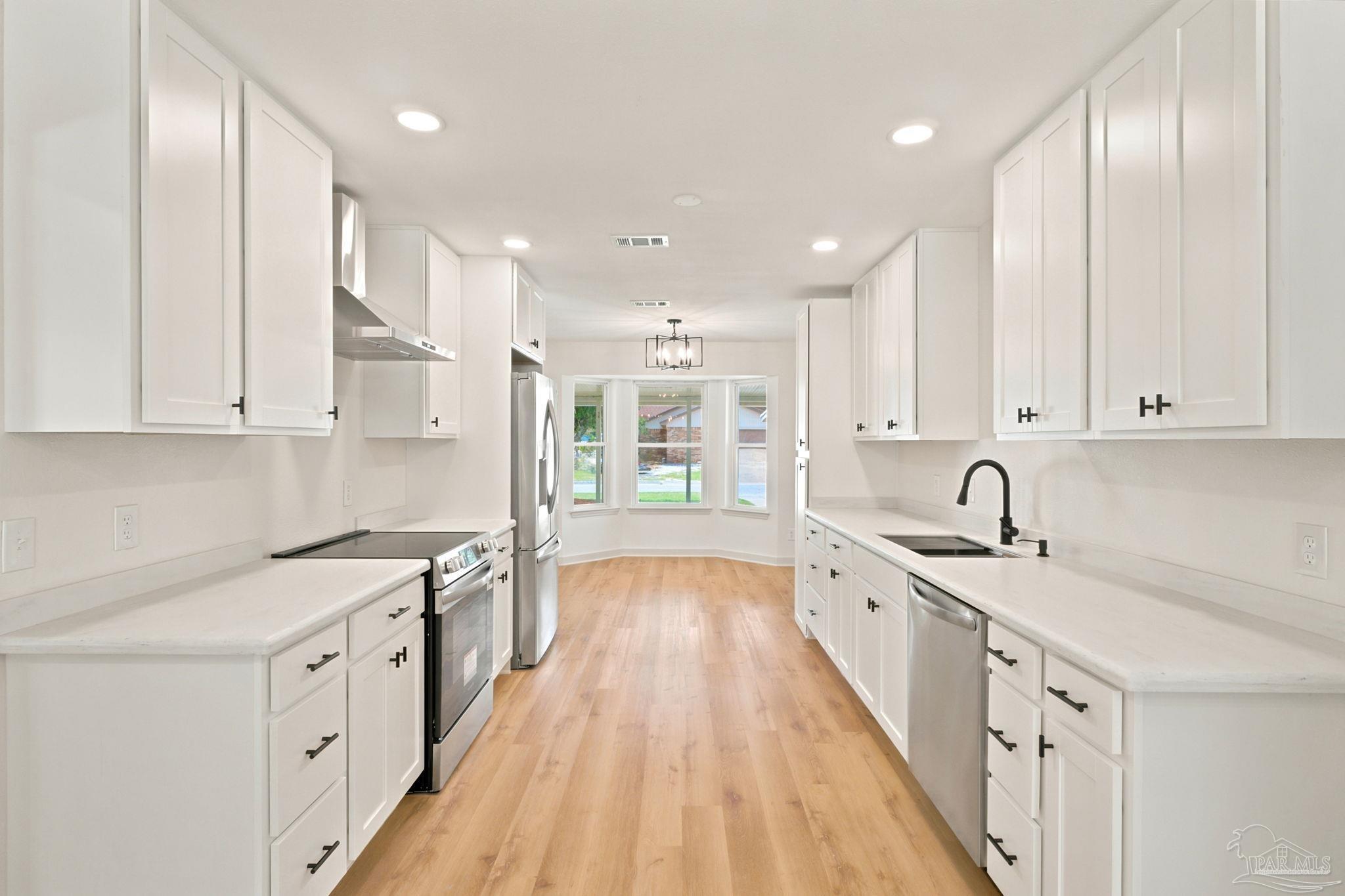 Bright white kitchen with stainless steel appliances, black fixtures, wood flooring, and a bay window.