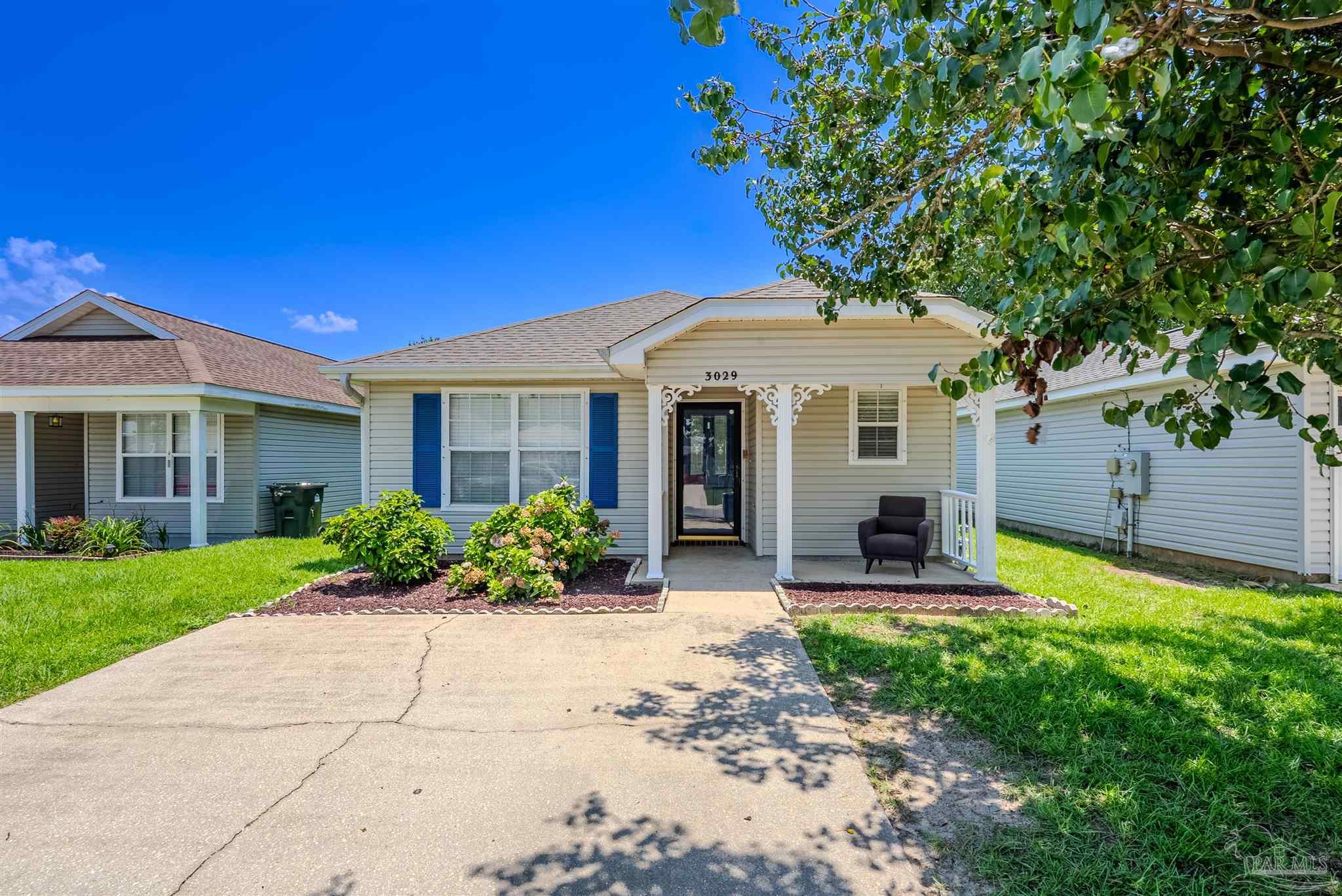 Single-story gray house with blue shutters, decorative covered porch, and landscaped front yard.