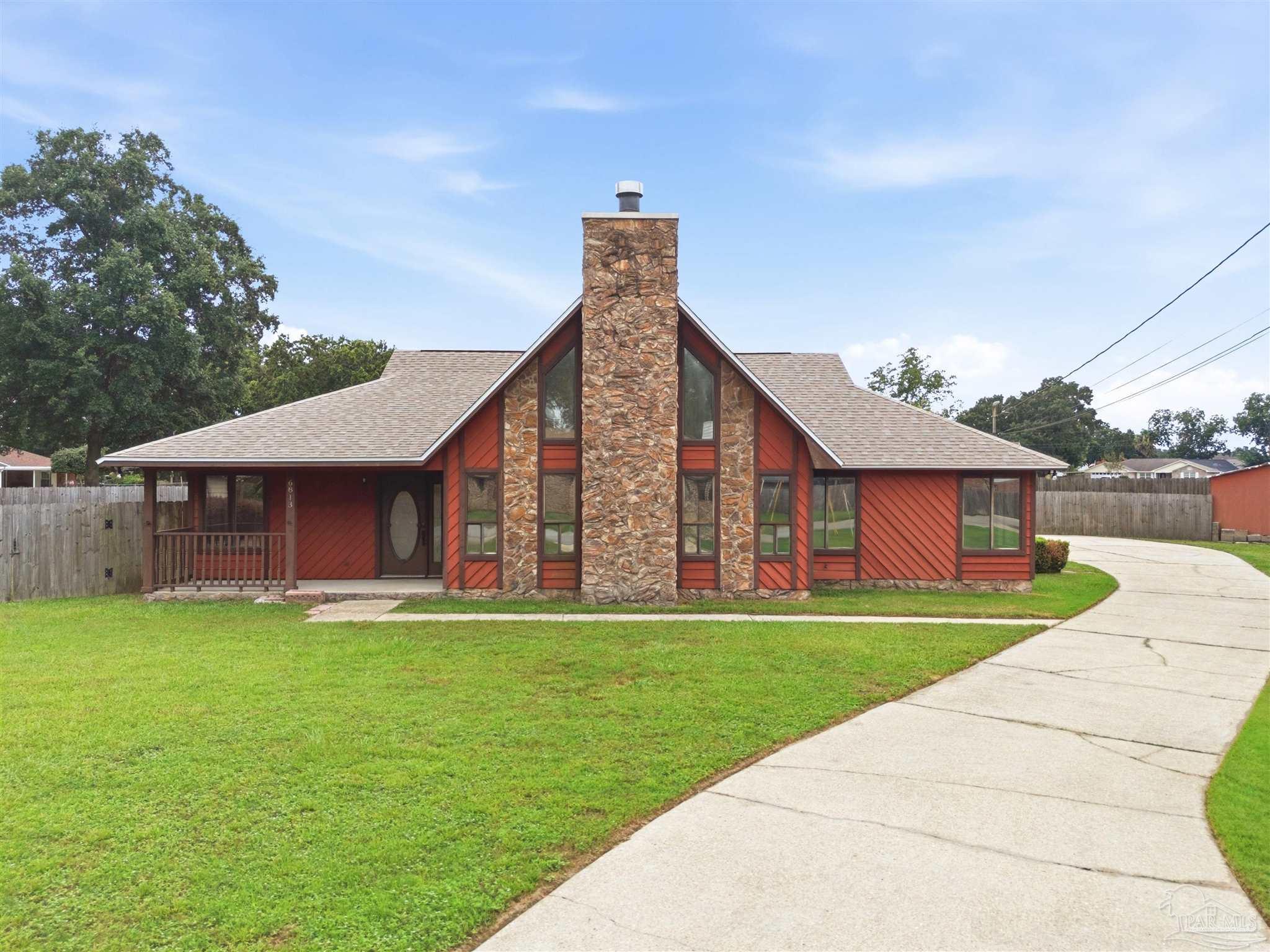 Red-sided house with a tall stone chimney, covered porch, and curved driveway.