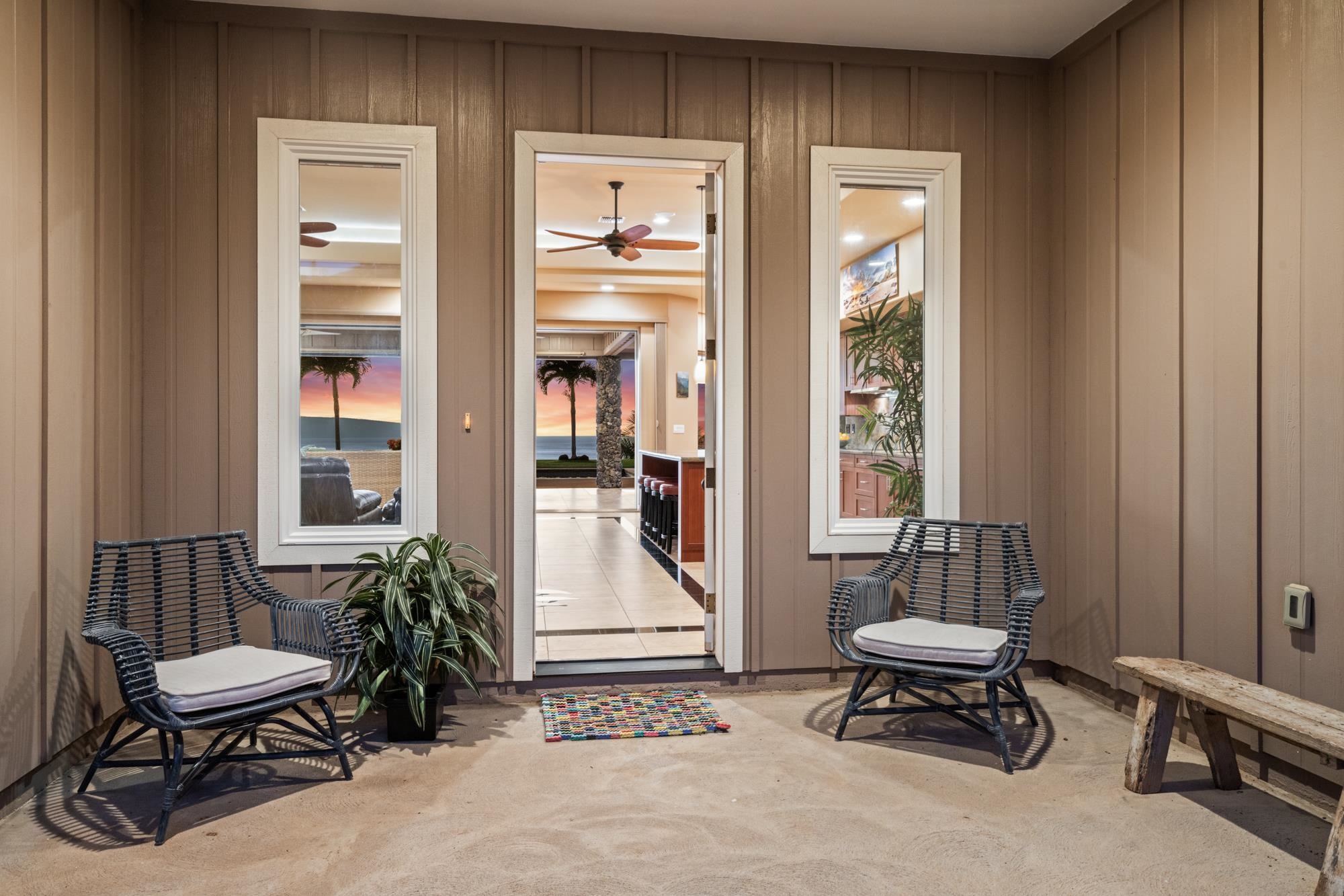 Covered lanai with woven chairs and a view through the home toward the ocean.
