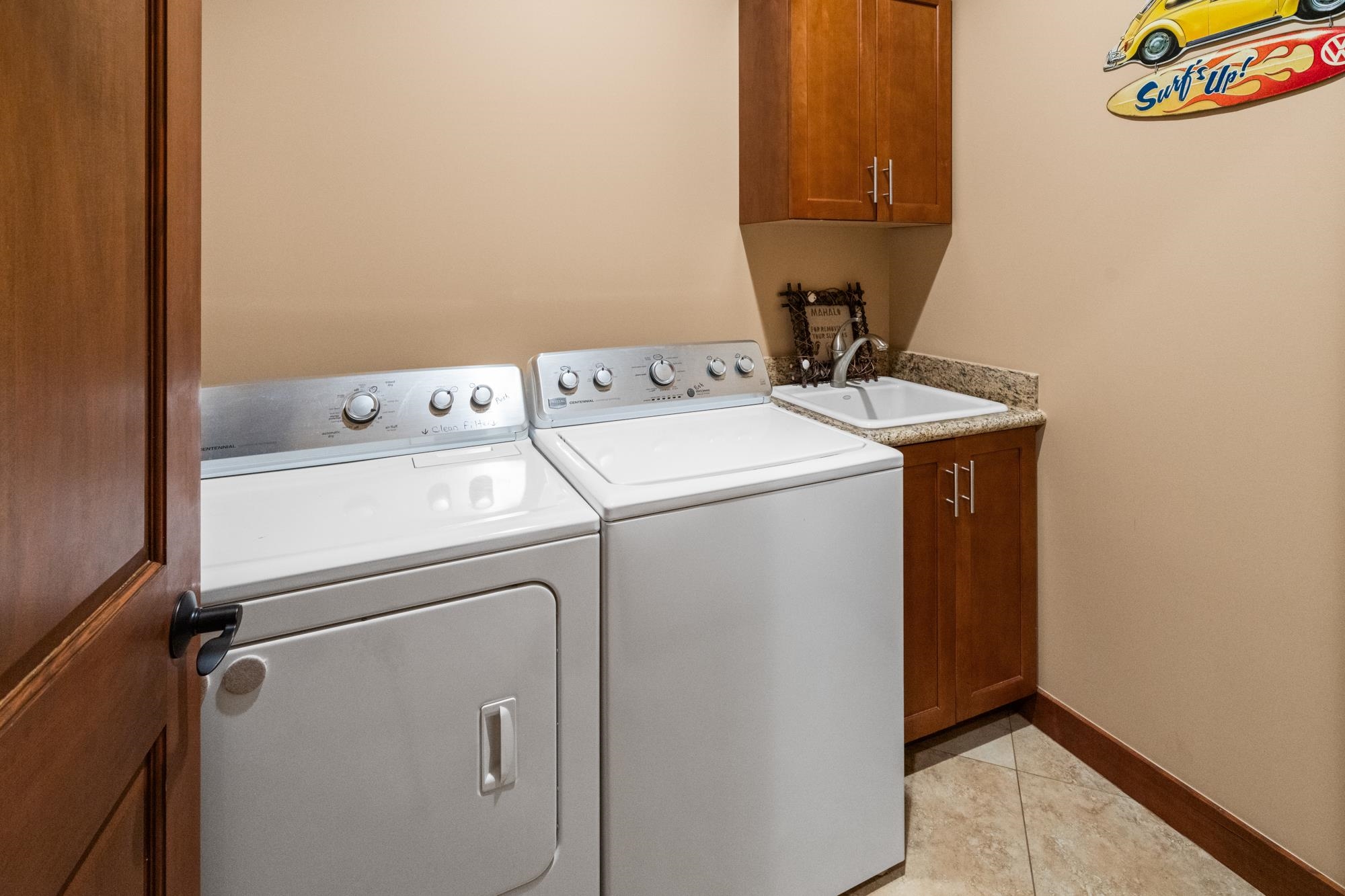 Laundry room with white washer and dryer, utility sink, granite countertop, and wood cabinets.