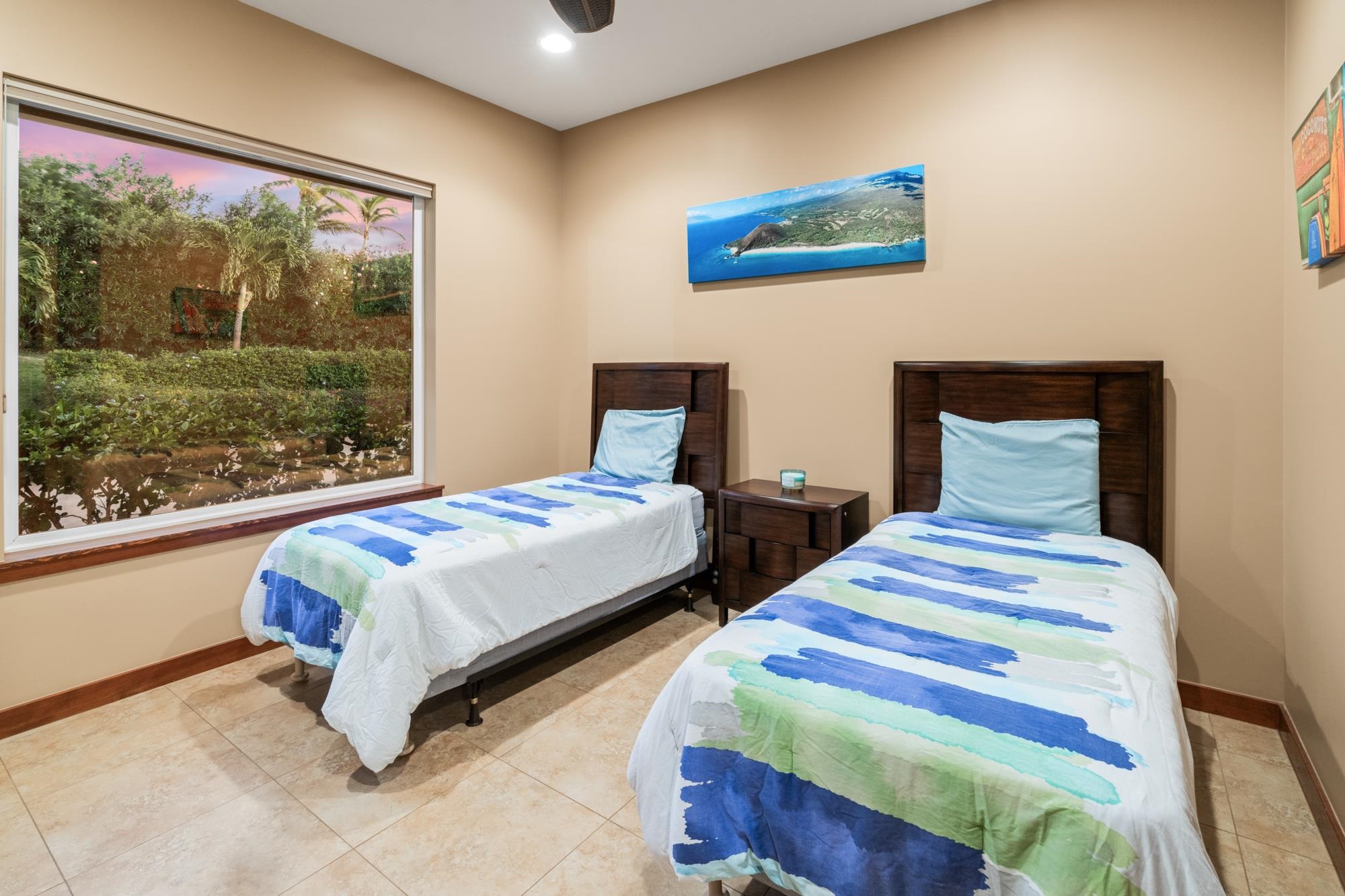 Twin bedroom with blue and green bedding and a large window overlooking a tropical garden.