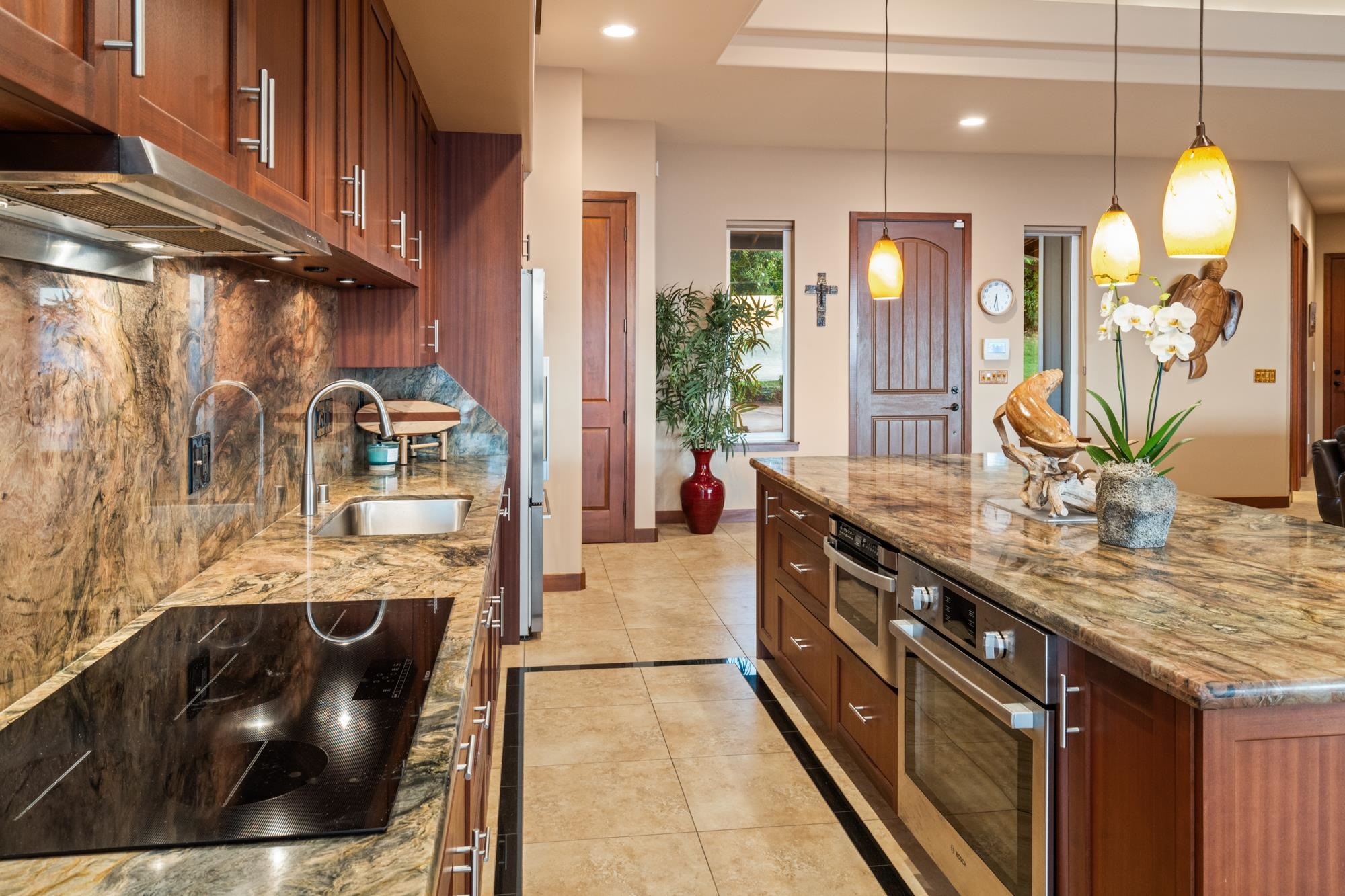 Kitchen with dark wood cabinetry, stone counters, a large island, and pendant lights.