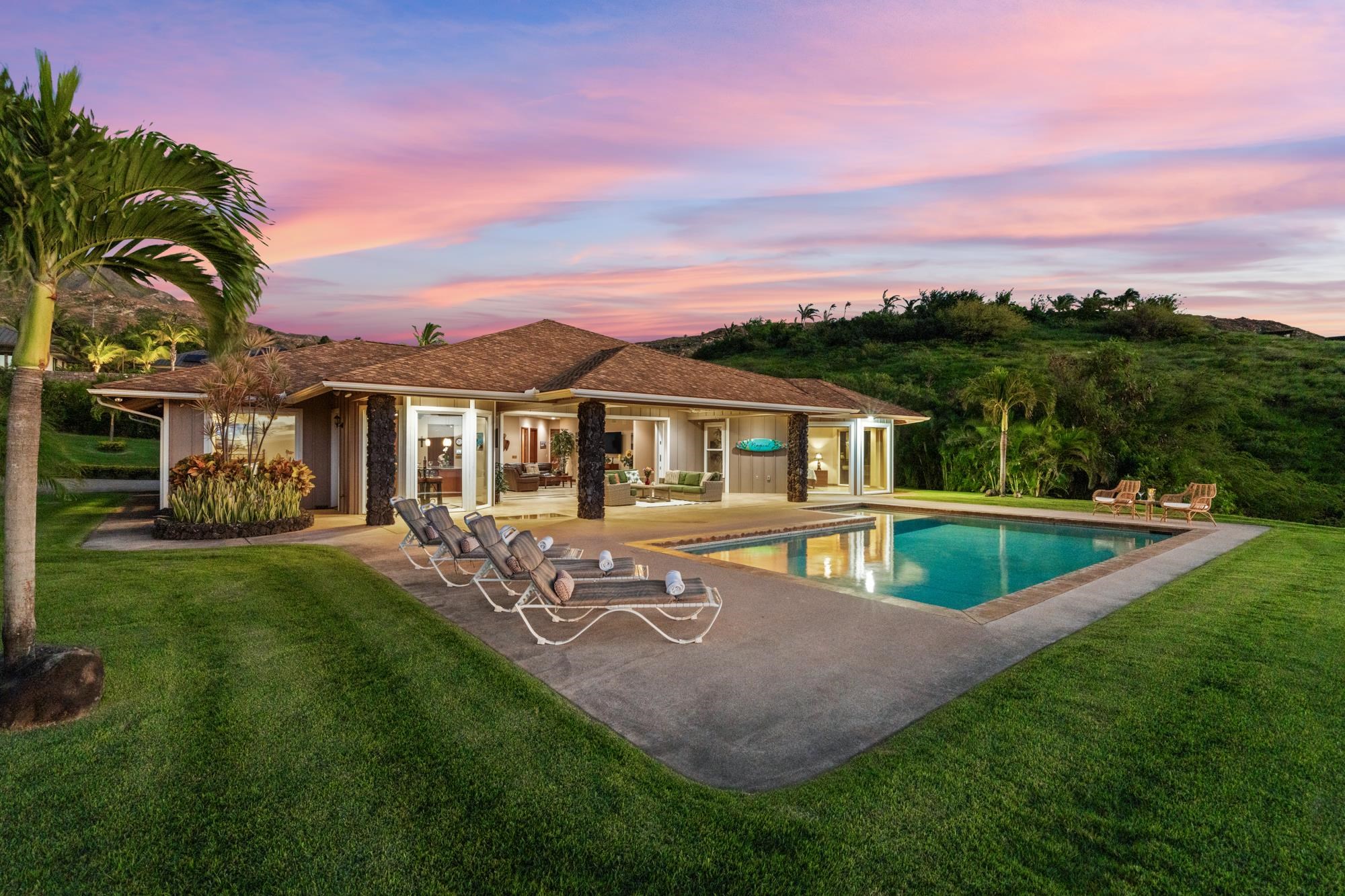 Single-story home and swimming pool at dusk, framed by palm trees beneath a pink sky.