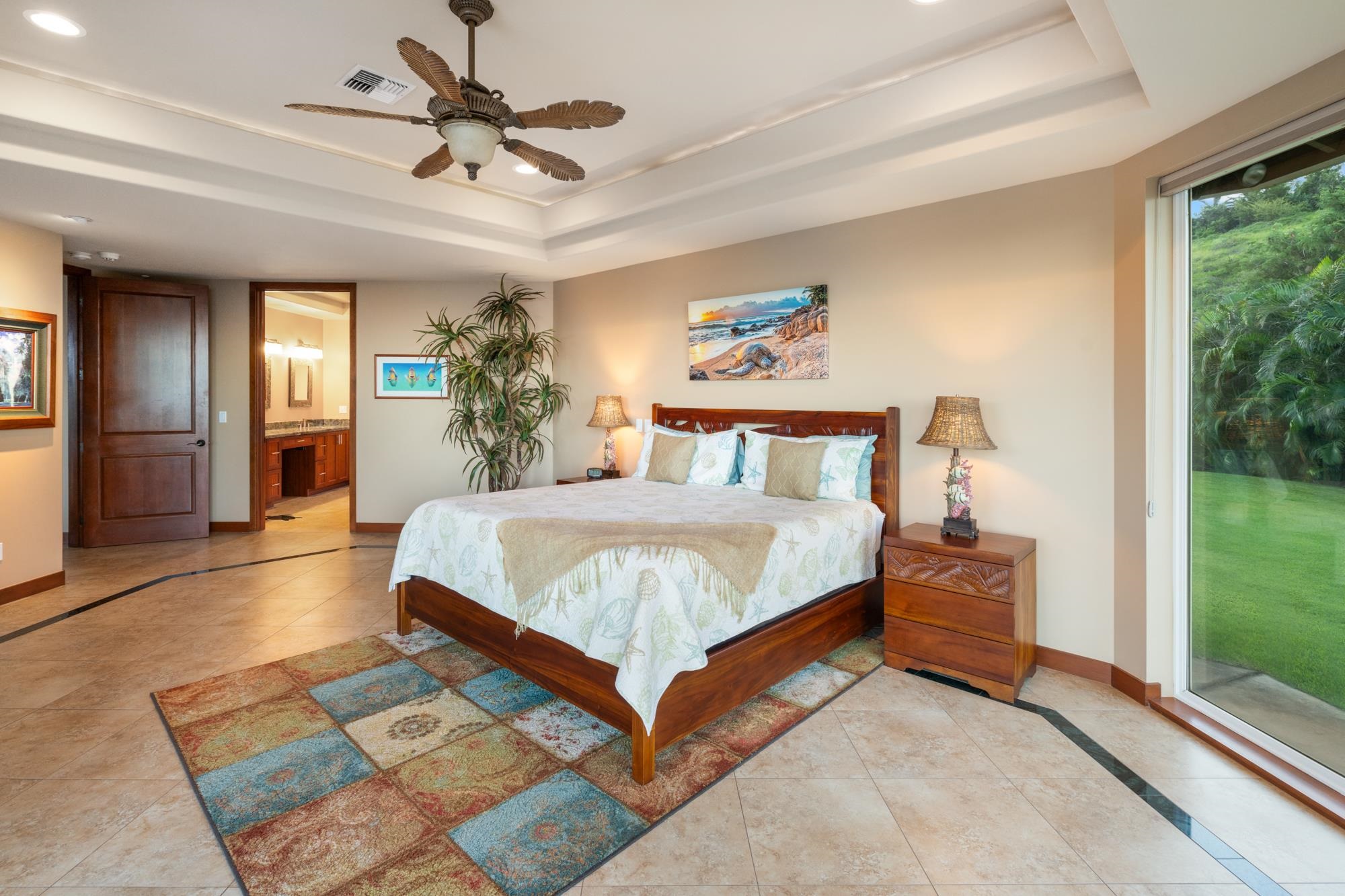 Furnished bedroom with a dark wood bed, tropical ceiling fan, and sliding glass door overlooking a lawn.