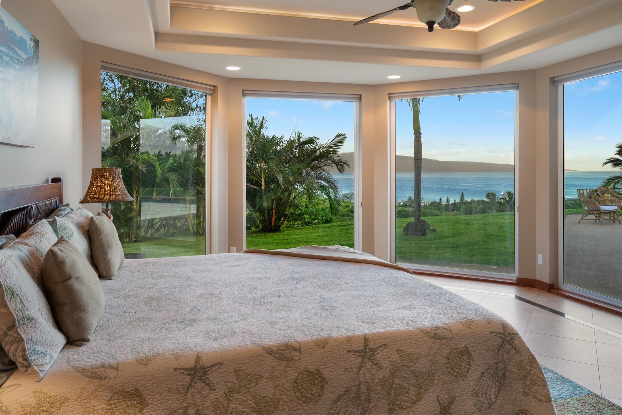 Bedroom with a large bed and wide ocean-view windows overlooking a palm-lined lawn.