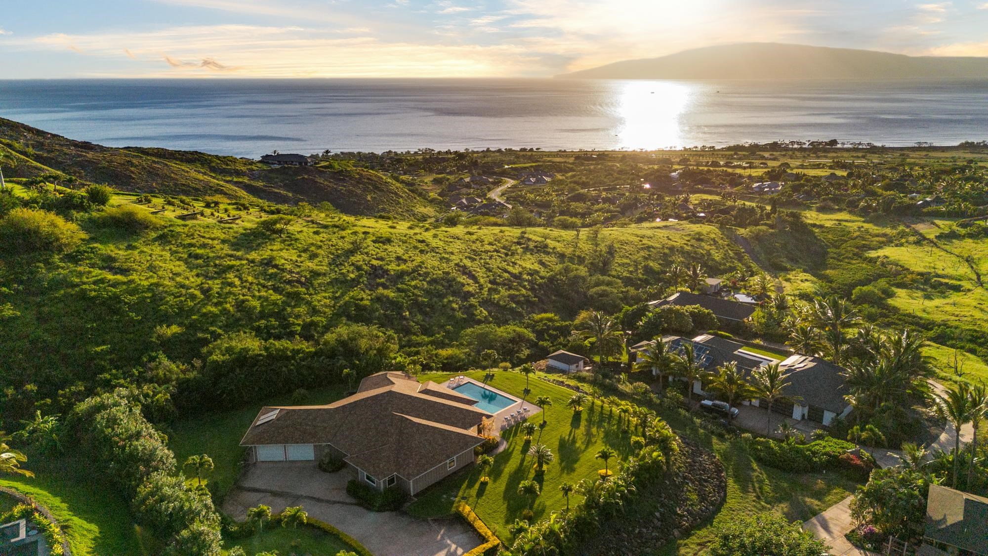 Aerial view of hillside homes and a pool overlooking the ocean at sunset.