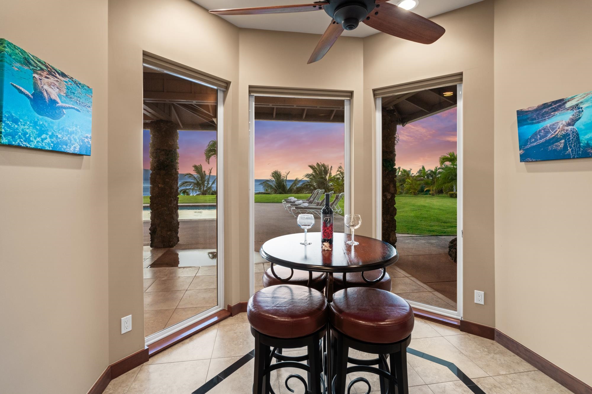 Dining nook with a round table and leather stools overlooking the ocean at sunset.