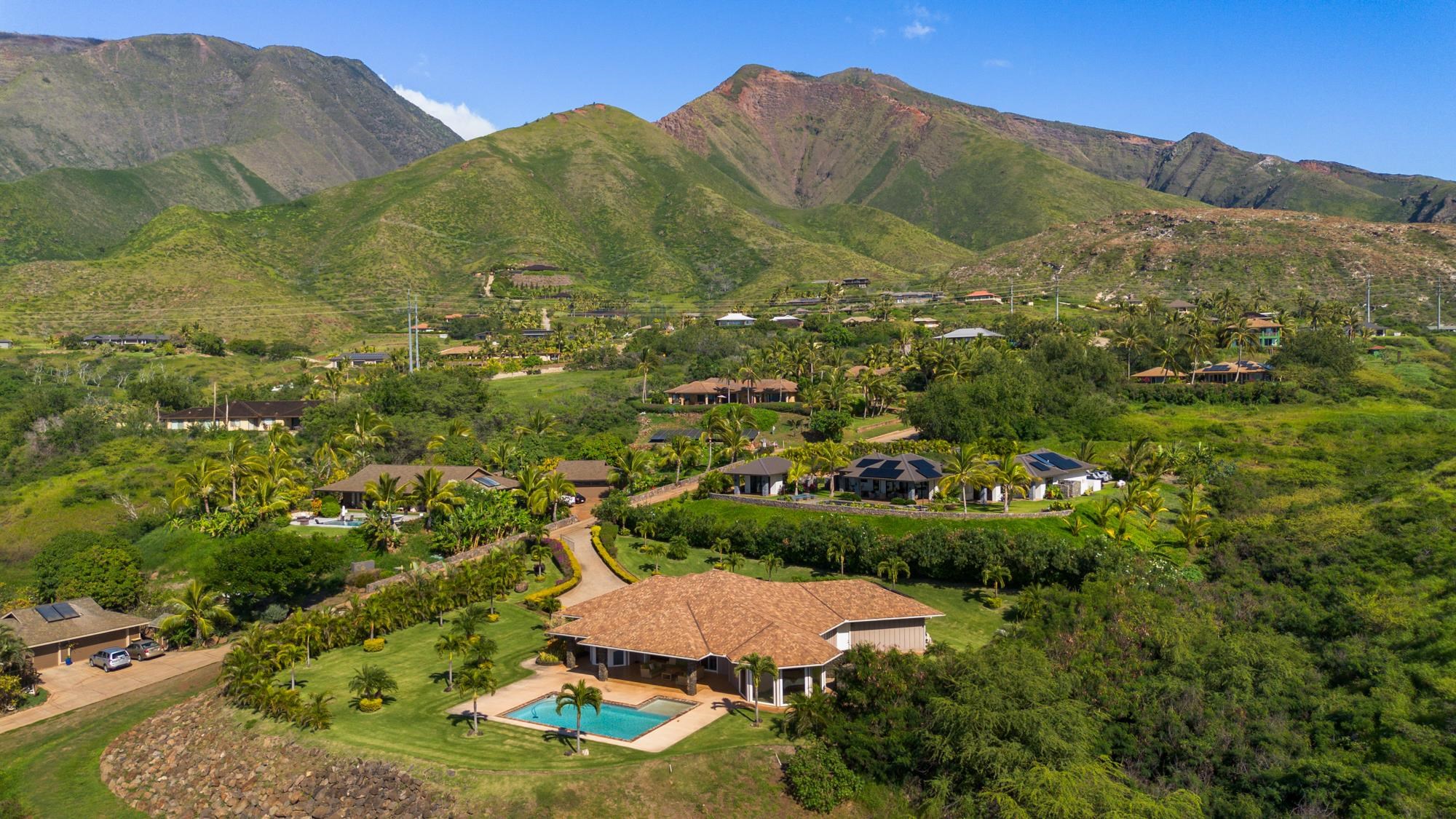 Aerial view of a home with a swimming pool, palm-lined grounds, and green mountains.