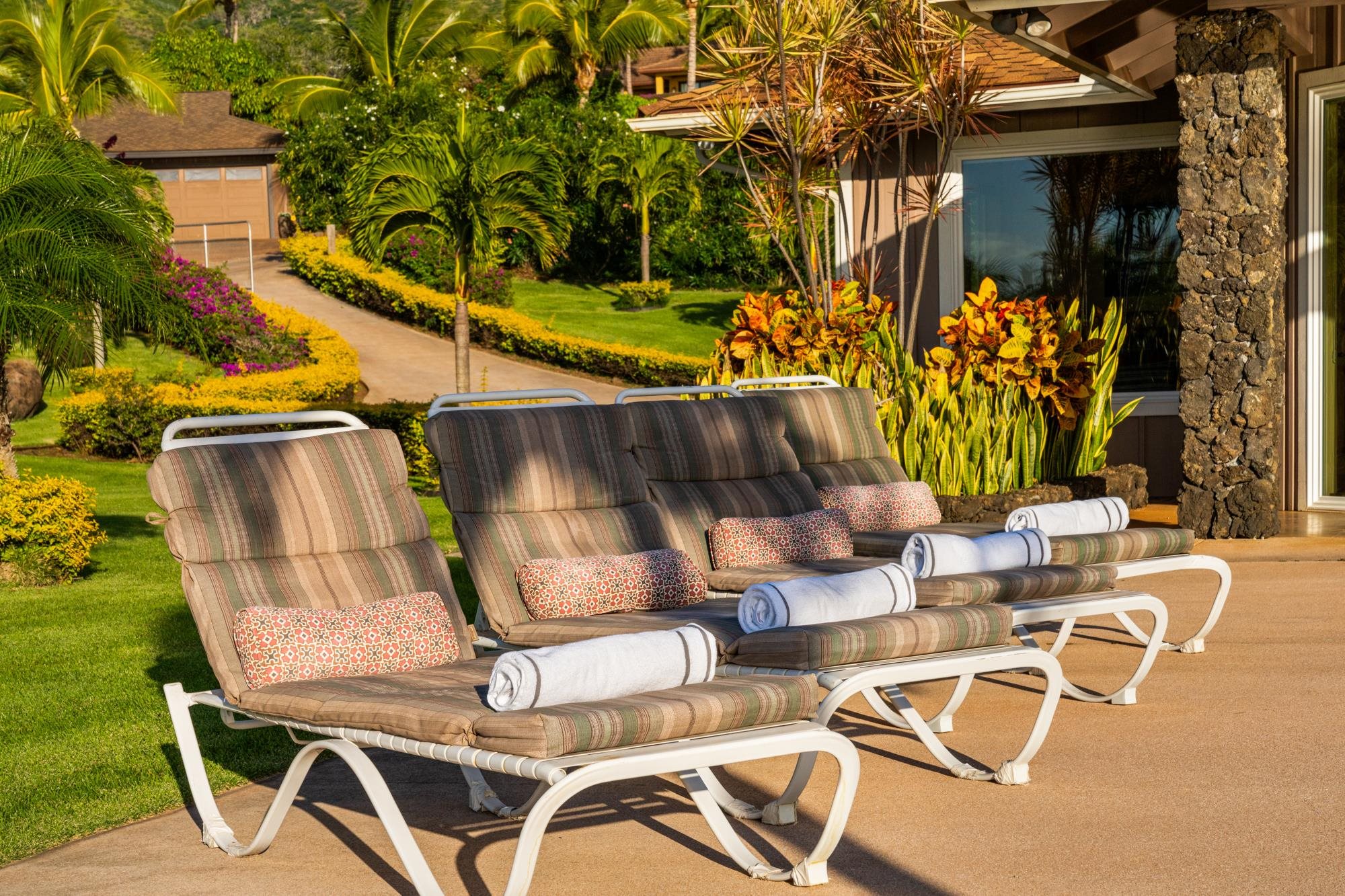 Patio with cushioned chaise lounges and rolled towels beside a lush tropical garden.