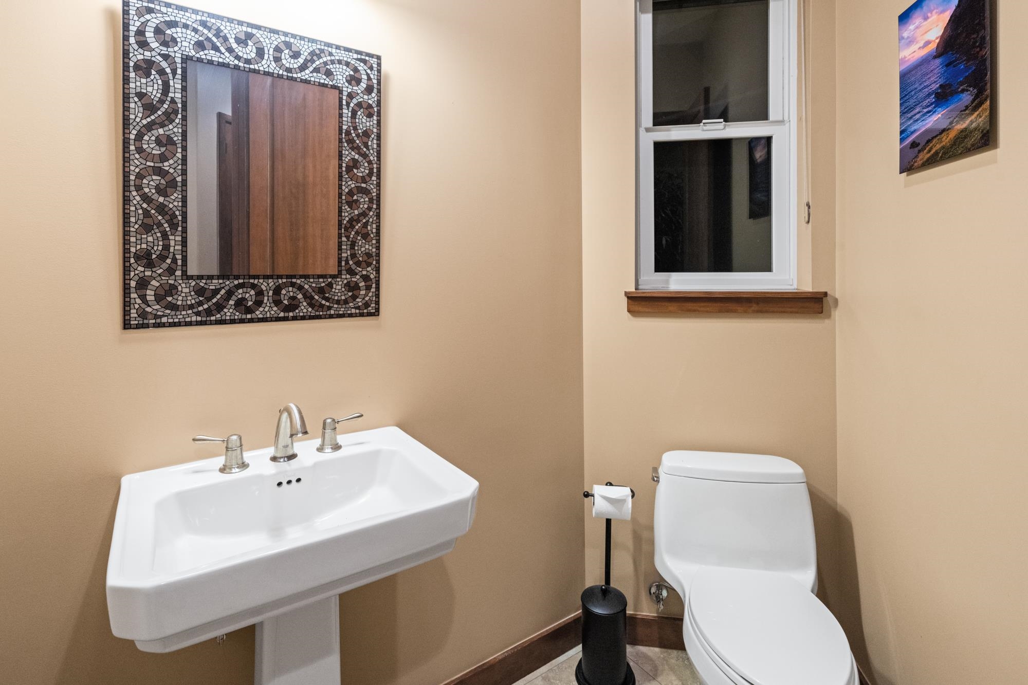 Bathroom with a white pedestal sink, toilet, and mosaic-framed mirror.