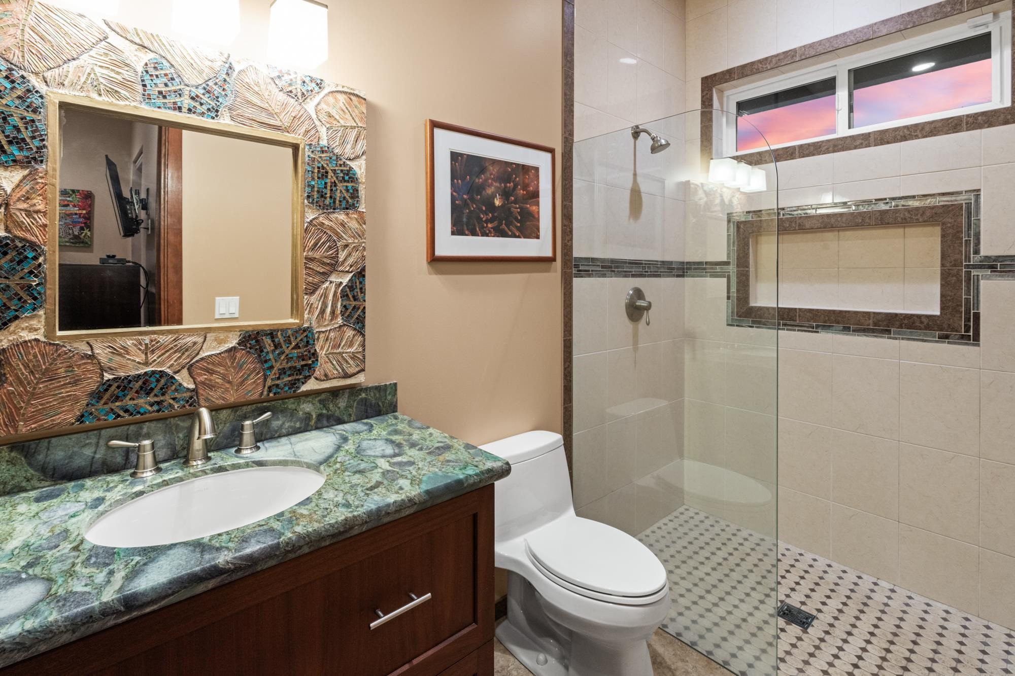 Bathroom with a glass shower, green stone vanity, and mosaic-framed mirror.