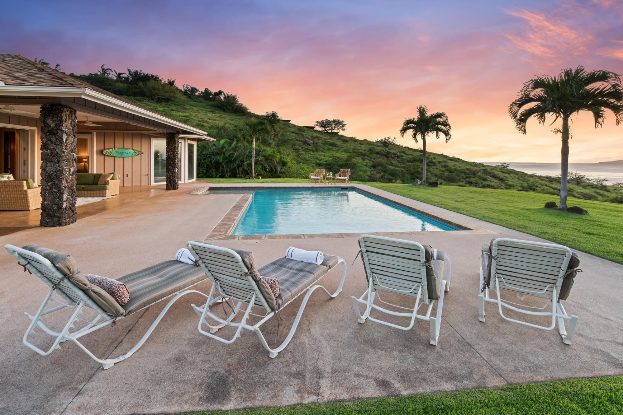 Pool terrace with lounge chairs, palms, and ocean views at dusk.