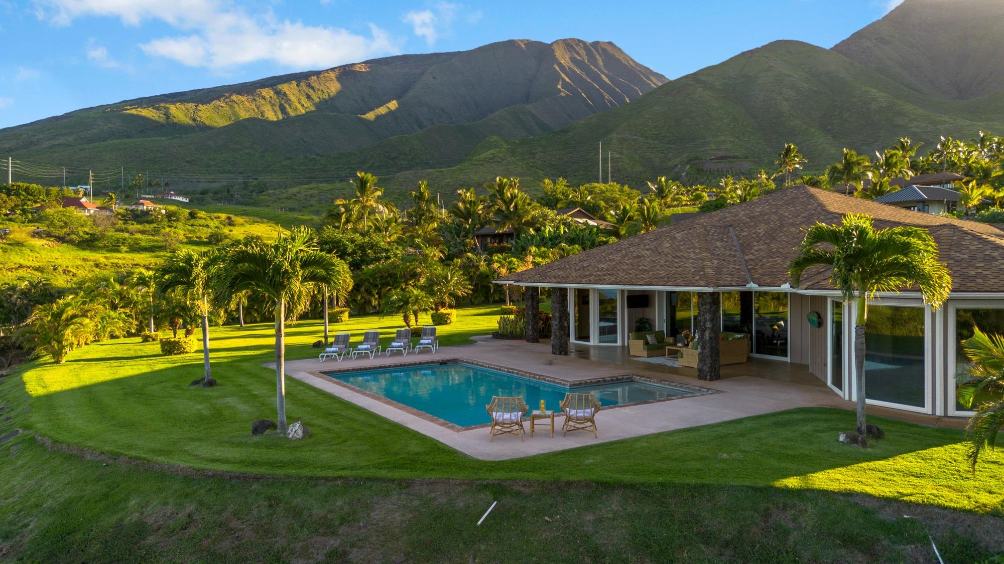 Tropical home and pool framed by palms, with green mountains rising behind the property.