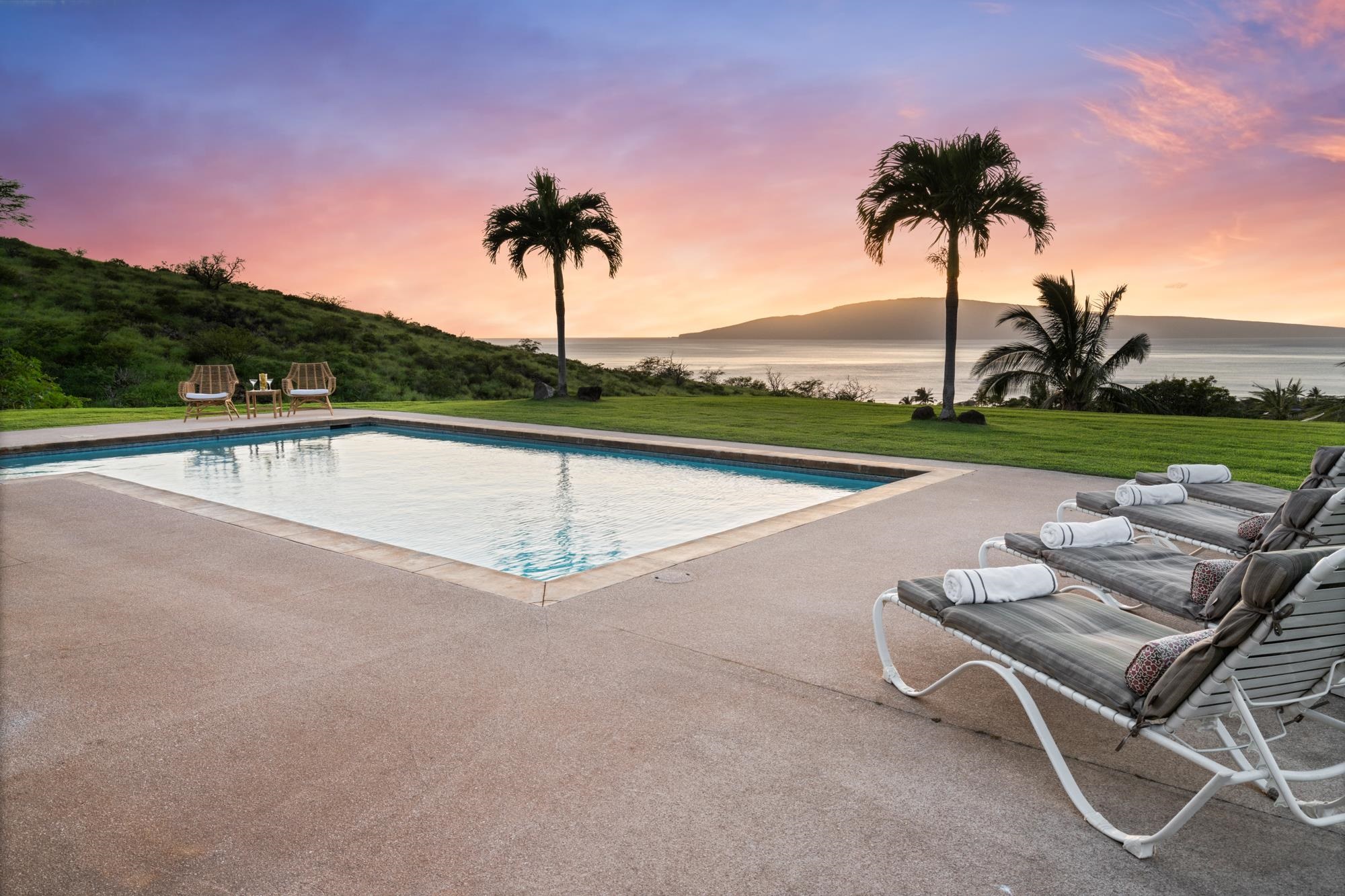 Poolside patio with lounge chairs overlooking the ocean at sunset.