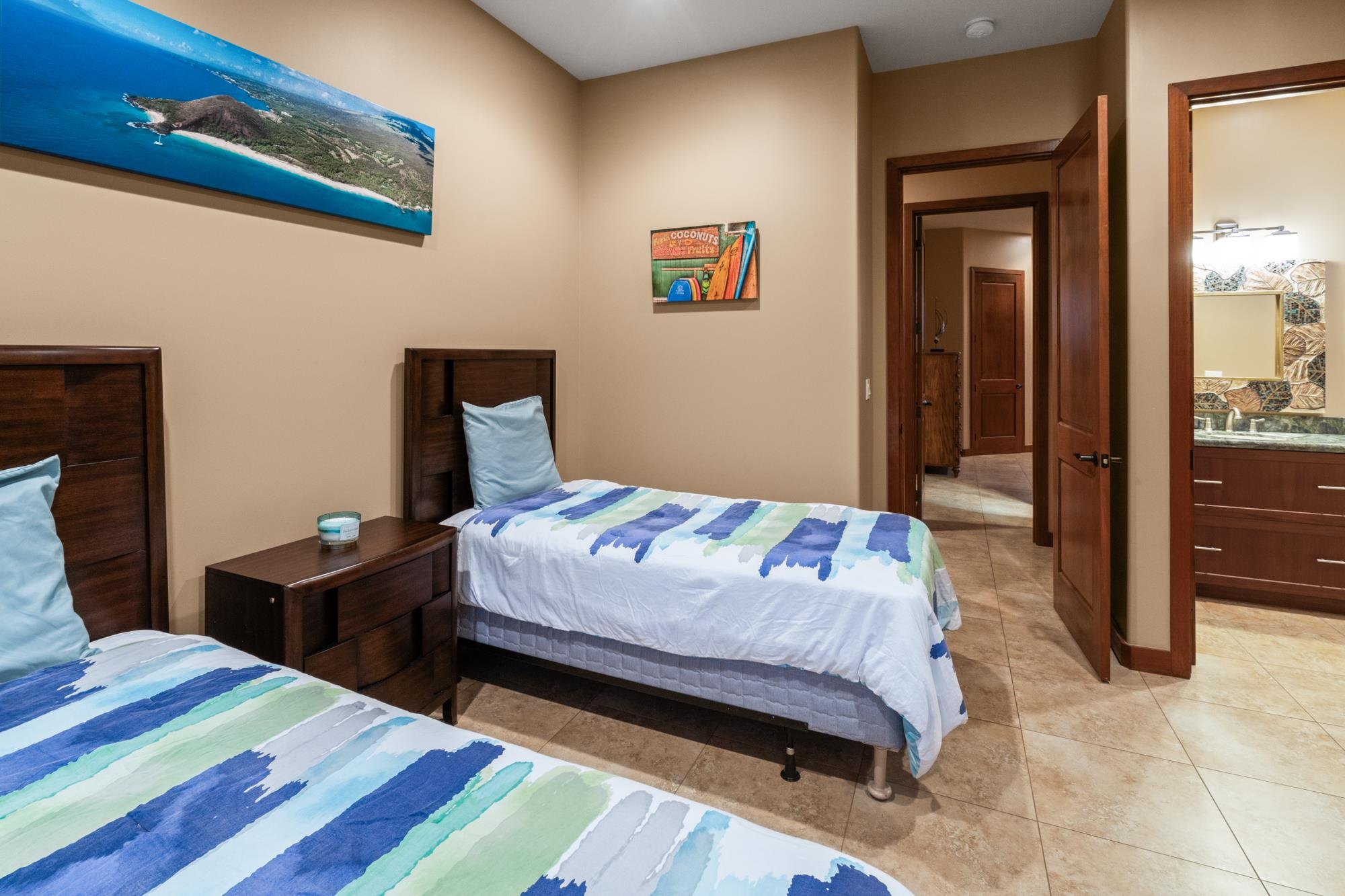 Bedroom with two twin beds, blue-green patterned bedding, dark wood furniture, and open doorways to a hall and bathroom.