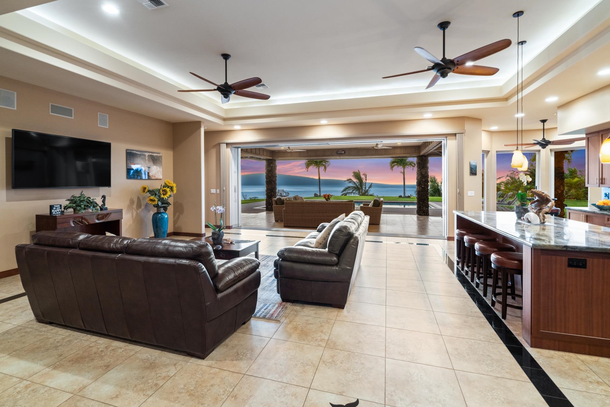 Open-plan living room opens to a patio and pool overlooking the ocean at sunset.