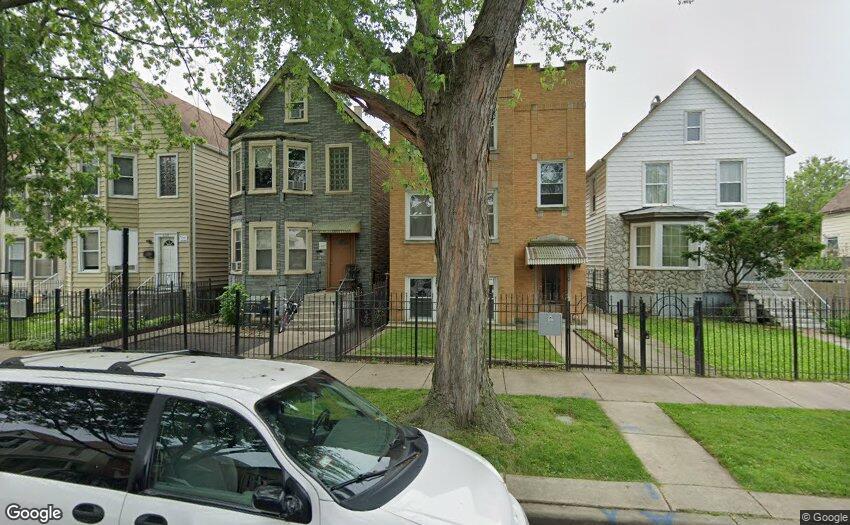 Brick-front home partly hidden by a large tree, with neighboring houses and fenced front yards.