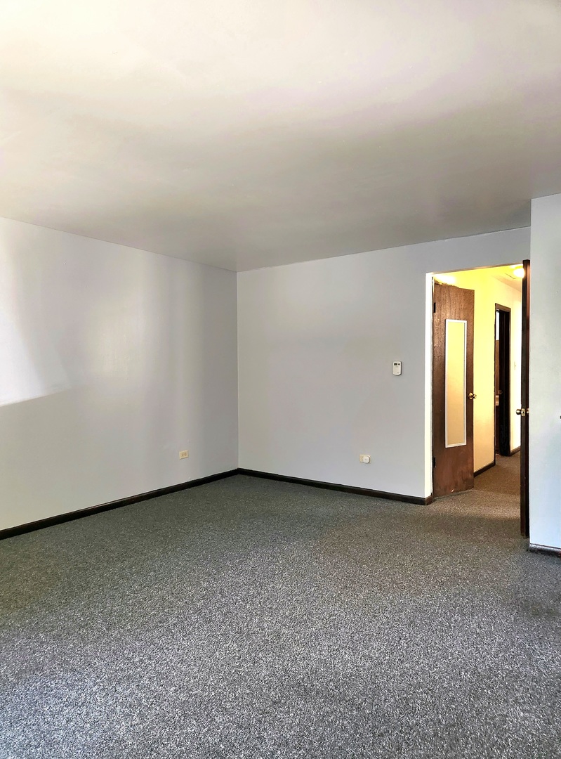 Empty carpeted room with white walls and an open wooden door to the hallway.