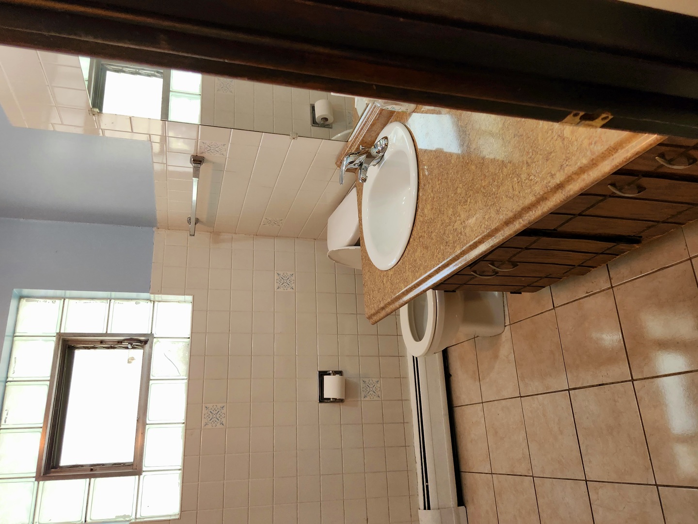 Bathroom with a brown vanity counter, white sink, tiled surfaces, and glass-block window.