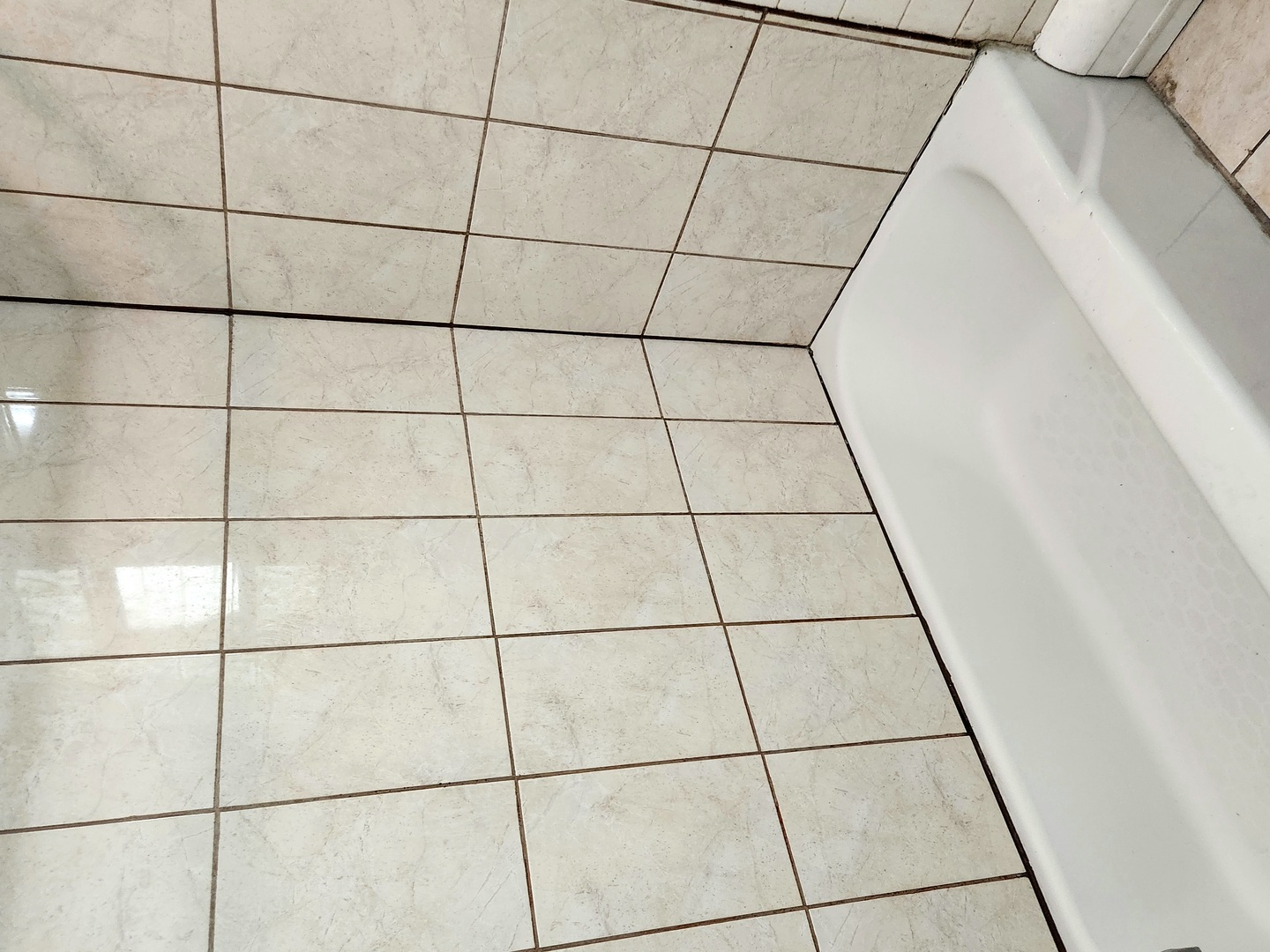 Bathroom floor with light square tiles beside a white bathtub.