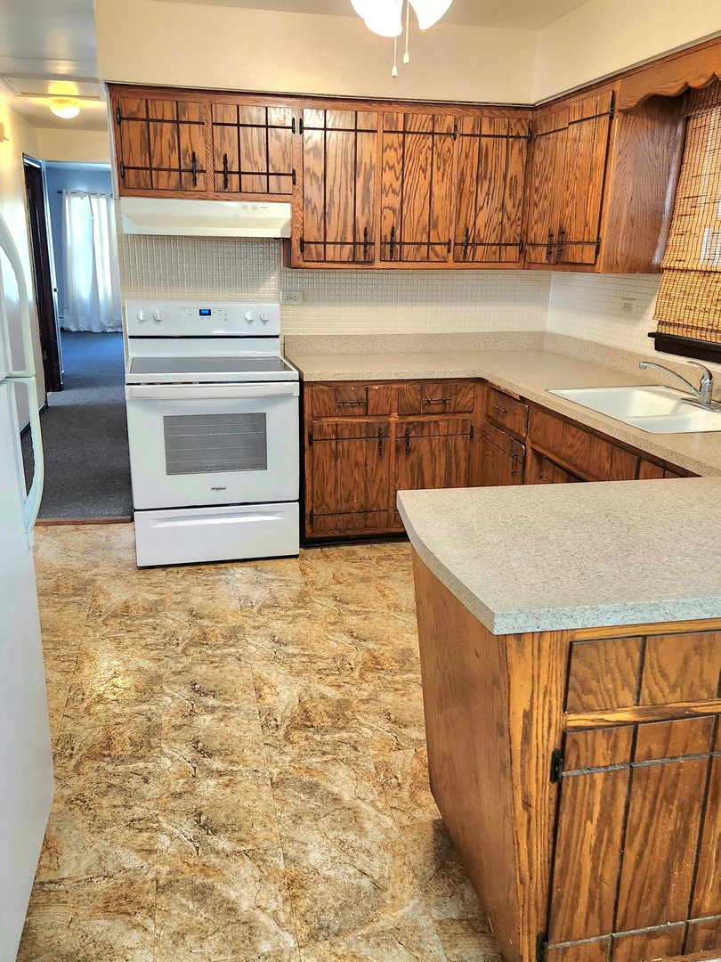 Kitchen with dark wood cabinets, a peninsula, white range, and patterned flooring.