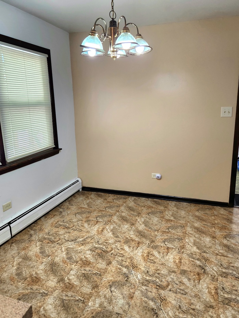 Empty dining area with a chandelier, window blinds, and patterned flooring.