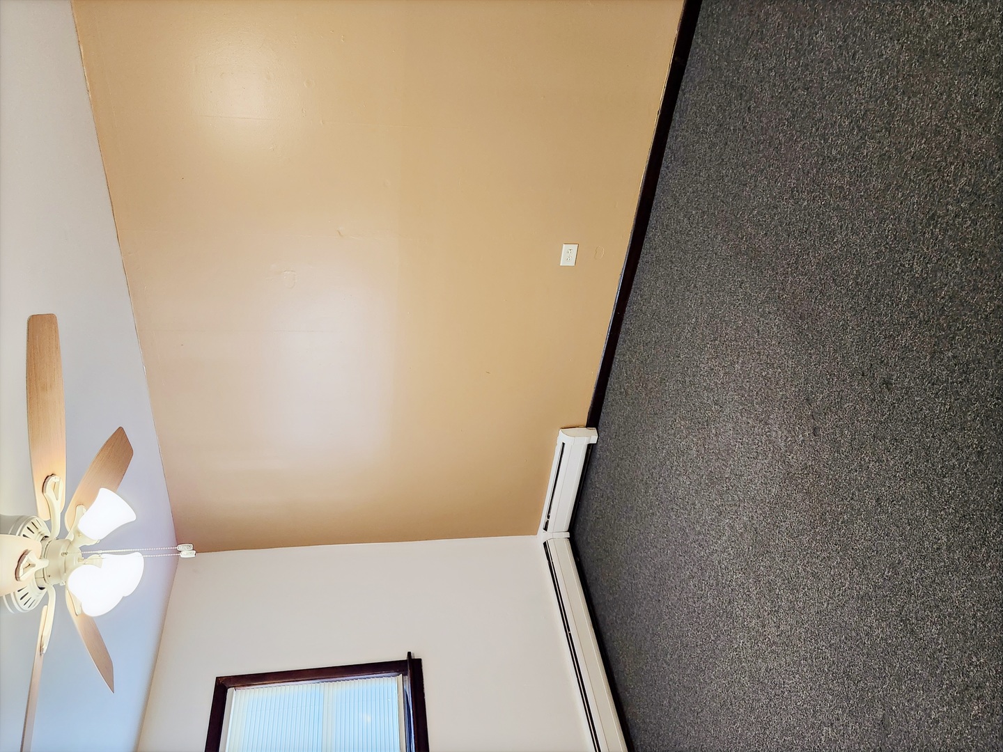 Room with a ceiling fan, dark gray carpeting, and a window with vertical blinds.
