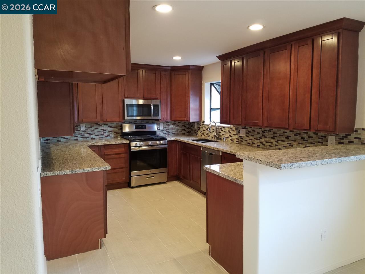 Kitchen with dark wood cabinets, granite counters, tiled backsplash, and stainless steel appliances.