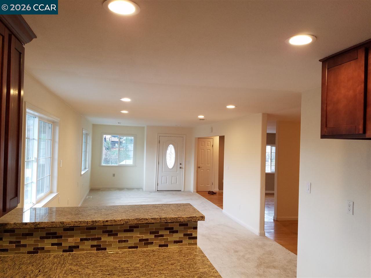 Open kitchen and entry area with granite counters, mosaic backsplash, and front door.