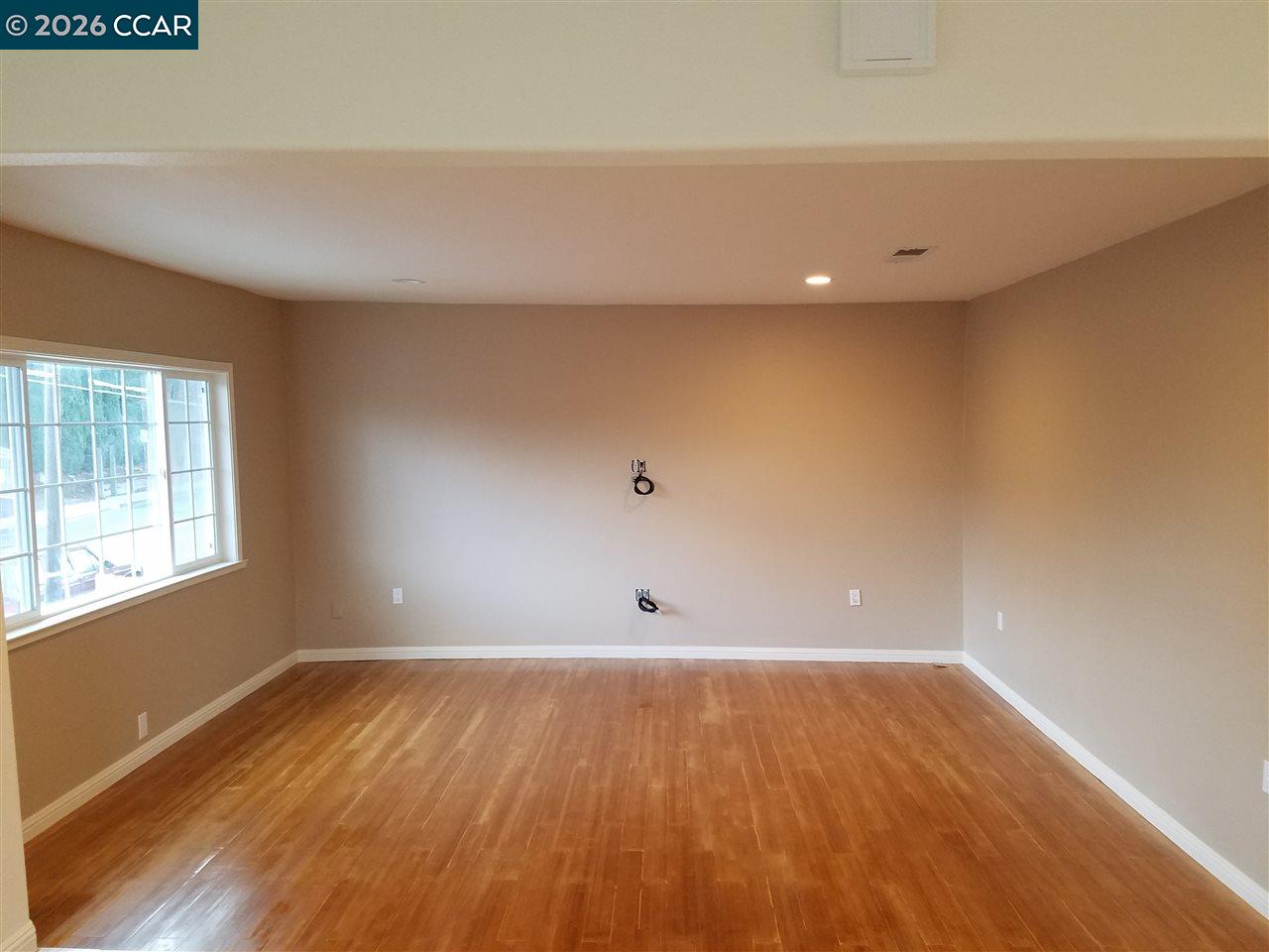 Empty room with polished hardwood floors, beige walls, and a large window.