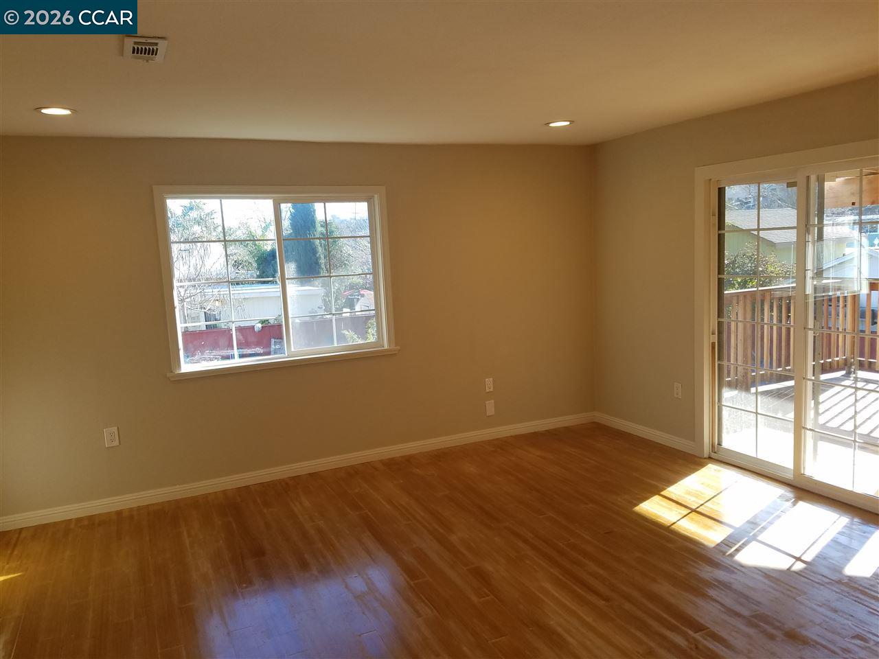 Empty living room with hardwood floors and sliding glass doors opening to a deck.
