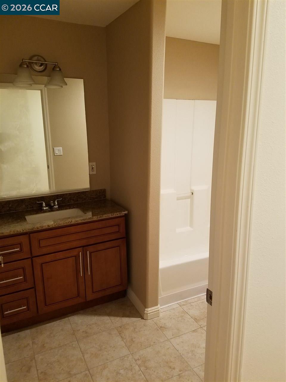 Bathroom with a dark wood vanity and granite counter beside a white bathtub.