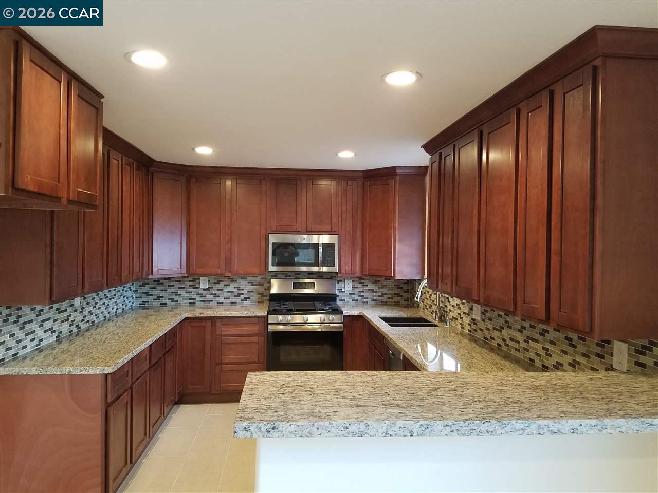 Kitchen with reddish-brown wood cabinets, granite counters, and a multicolored tile backsplash.
