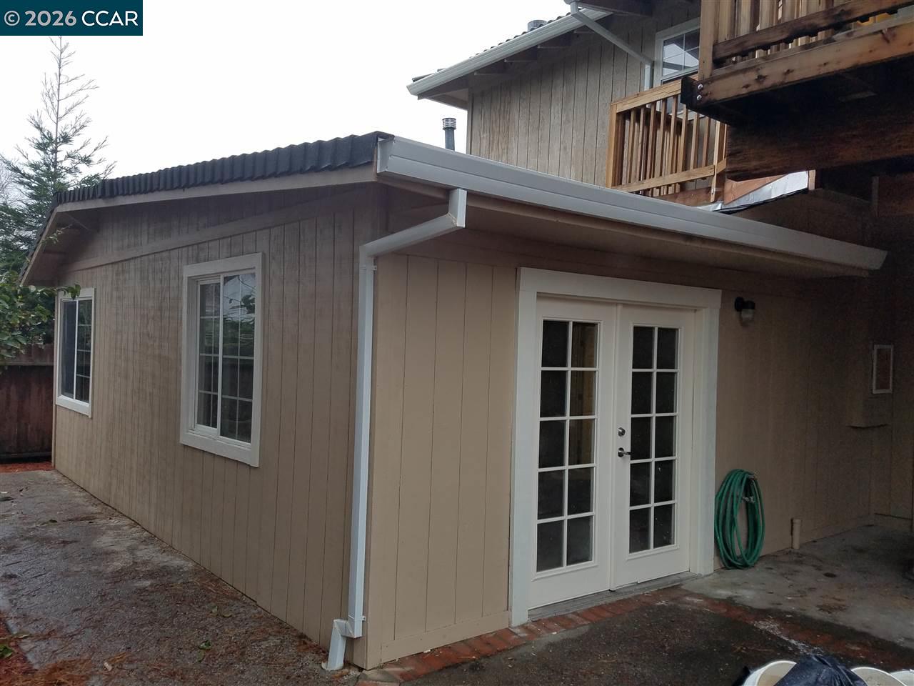 Backyard outbuilding with white French doors beneath a raised wooden deck.