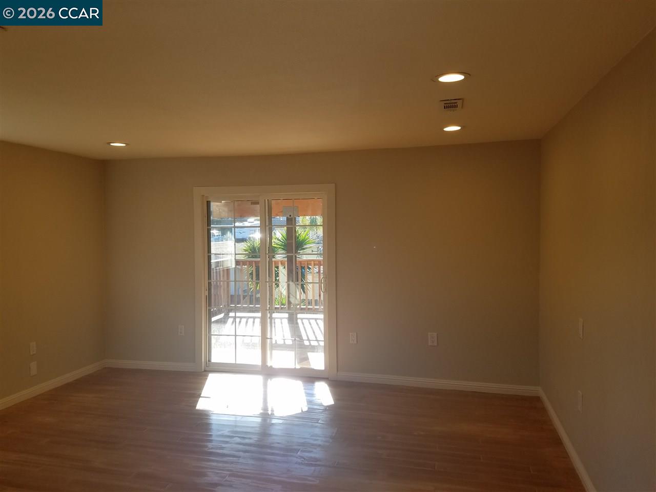 Empty room with wood flooring and sliding glass doors opening to a deck.