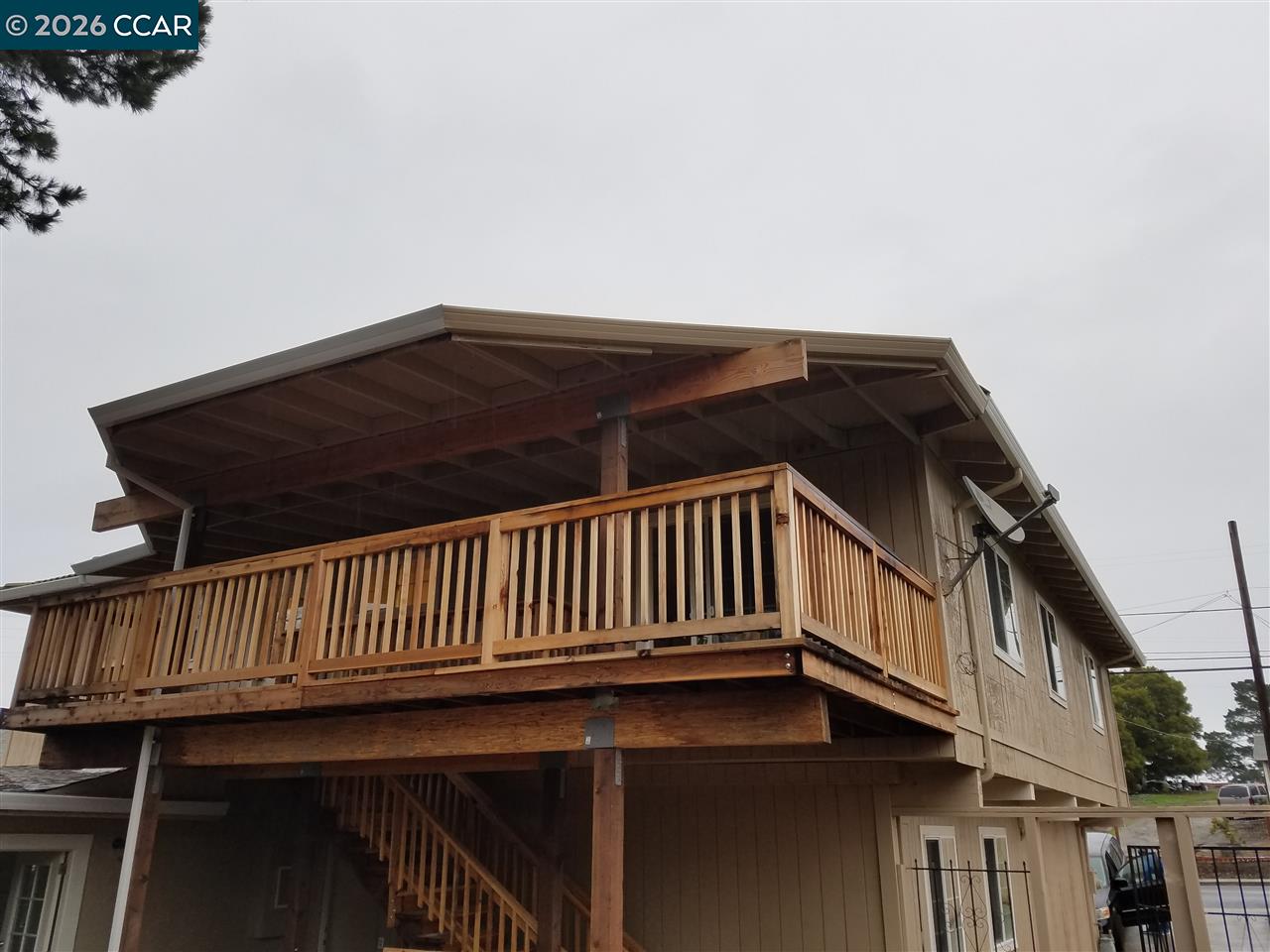 Two-story home's exterior with a large raised wooden balcony and exposed roof framing.
