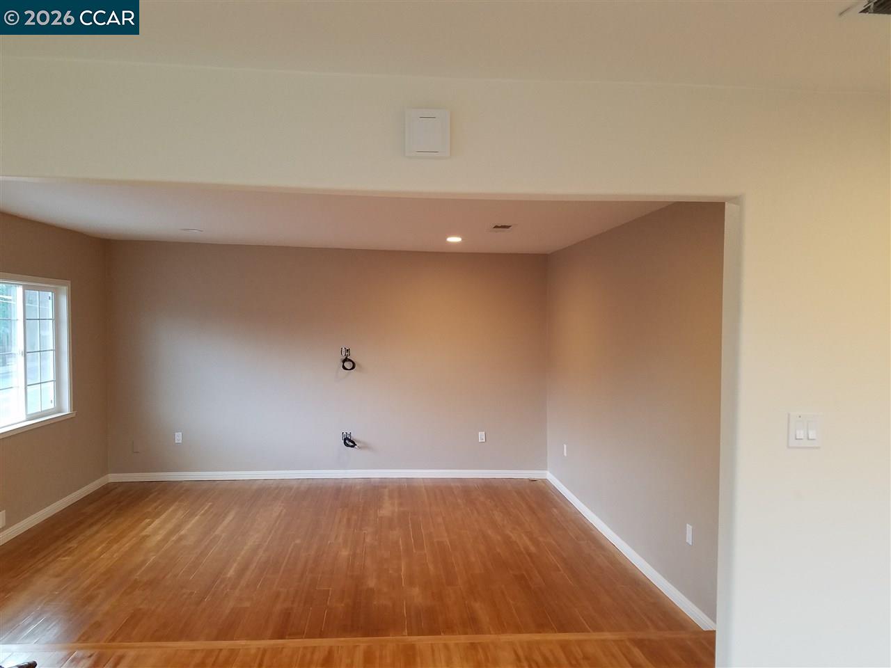 Empty living room with hardwood floors and television hookups on the far wall.