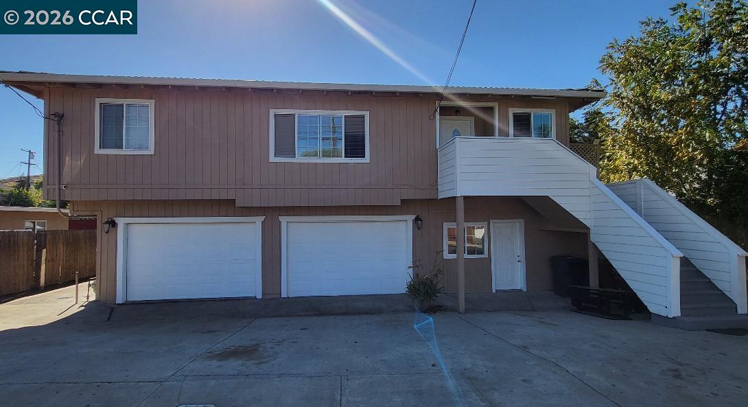 Brown two-story home with two garage doors and a prominent white exterior staircase.