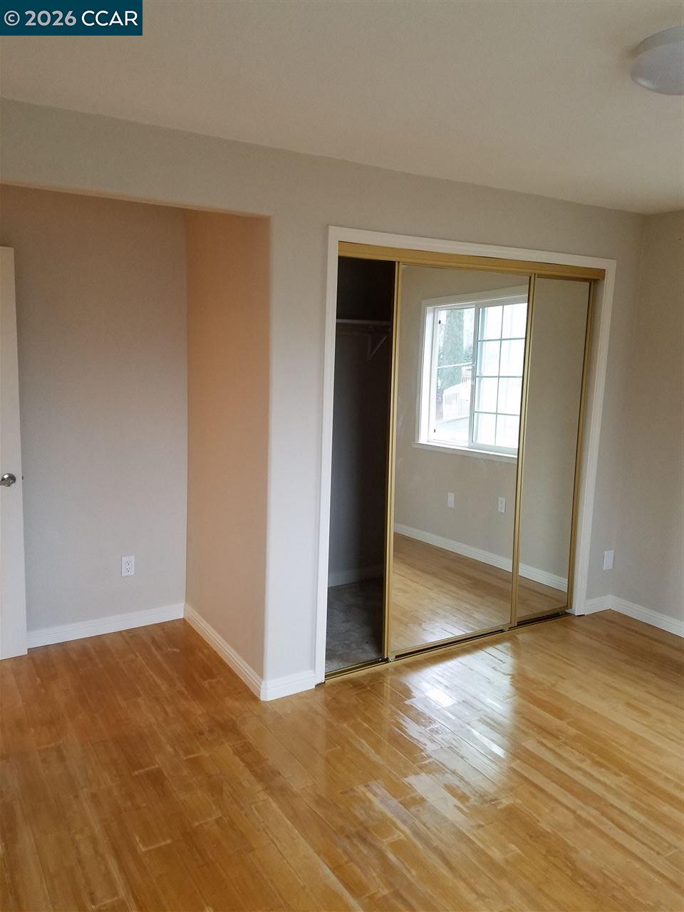 Empty bedroom with polished hardwood floors and a mirrored sliding closet door.